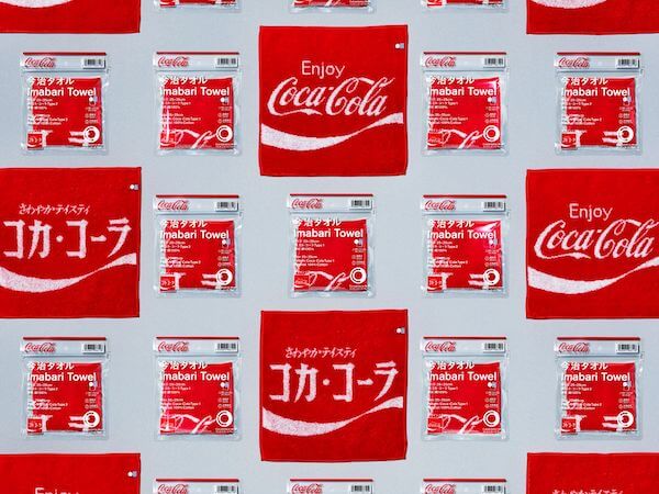ファミリーマートが「ファセッタズム」の落合宏理監修の「コカ･コーラ」ロゴの今治タオルを発売